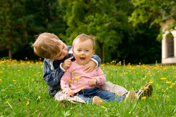 Happy baby girl and young brother sat in together in field.