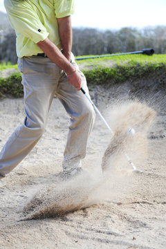 A professional golfer playing a shot out of a sand-trap.