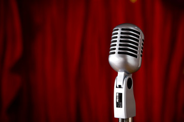 A silver vintage microphone in front of a red stage curtain