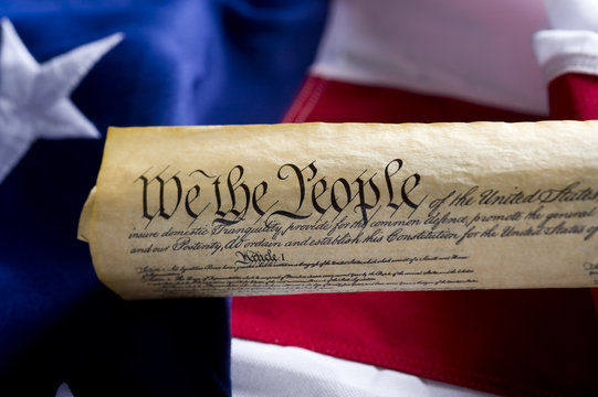 A copy of the USA Constitution scroll in front of a  Flag