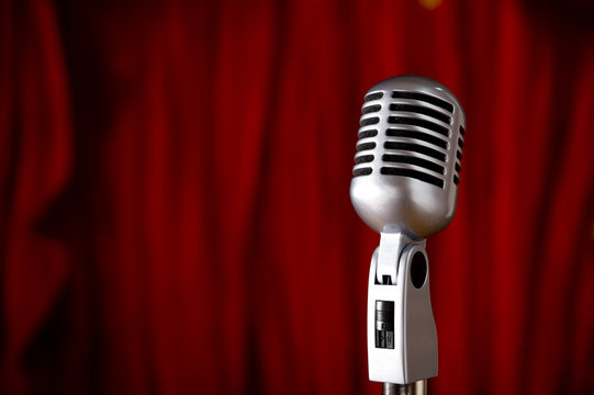 A silver vintage microphone in front of a red stage curtain