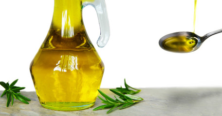 Olive oil in a glass container and spoon, with fresh rosemary