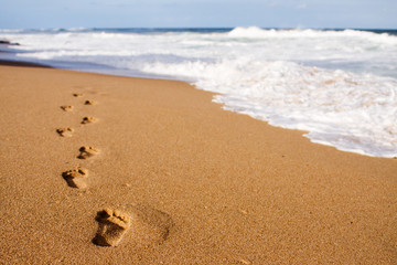 Human footprints leading away from the viewer into the sea - Powered by Adobe
