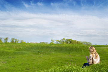 Naklejka premium Girl sits on a grass and hold look far away