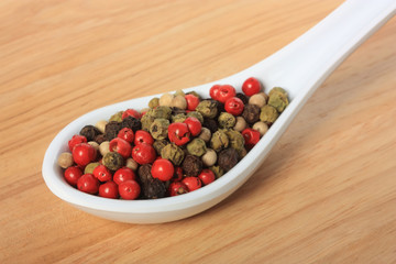 Spoon with four pepper kinds on wooden board
