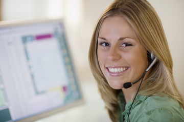 Smiling woman with headset and computer monitor - obrazy, fototapety, plakaty