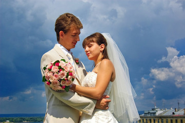 Groom with the bride on the cloudy sky background.
