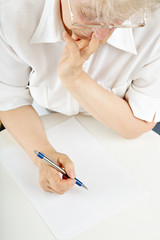 The elderly woman writes something on a sheet of paper