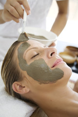 woman havin mud mask applied to her face by professional