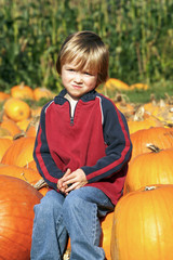 Cute young boy sitting on a pumpkin at the pumpkin patch