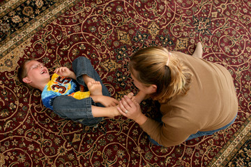mother tickling her son's bare feet on the floor