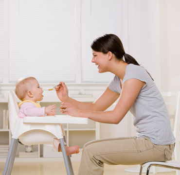 Mother feeding hungry baby in highchair in kitchen