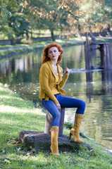 beautiful woman sitting near river in yellow casual autumn