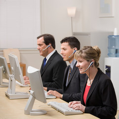 Co-workers in headsets working at computers in call center