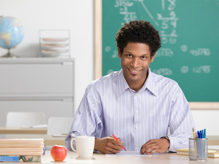 Happy teacher grading papers in school classroom