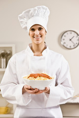 Chef in toque proudly holding bowl of spaghetti and tomato sauce