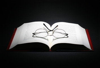 open book with a pair of eye glasses on dark background.