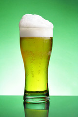 Glass of beer with froth over green background