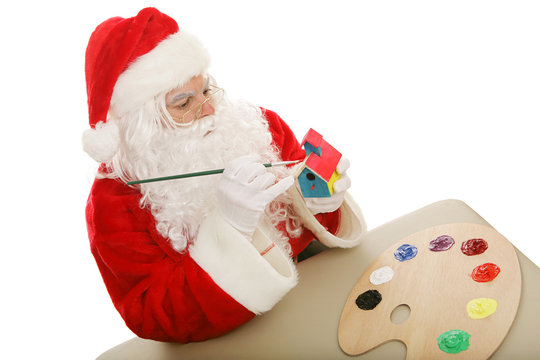 Santa Clause in his workshop, painting a toy.  Isolated