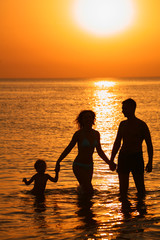 Parents with child in sea on sunset