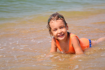 Little girl lies in waves on shore