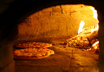 Pizzas baking in an open firewood oven