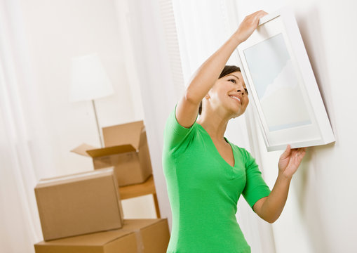 Happy woman moving into new home hanging picture on wall