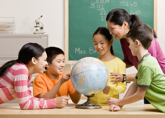 Teacher and students viewing globe in geography classroom