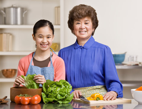 Granddaughter preparing salad with grandmother in kitchen