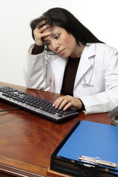 Tired  Stressed Doctor With Head In Hands Sitting At Computer.