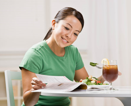 Happy woman eating healthy lunch while reading magazine