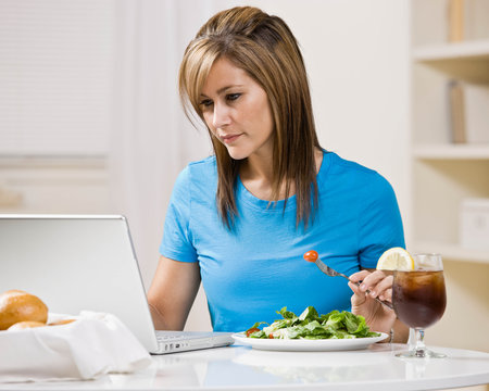 Woman eating healthy lunch while typing on laptop