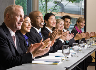 Multi-ethnic co-workers sitting in a row, applauding at table