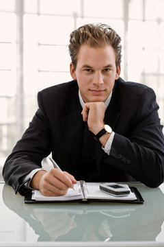 Businessman sitting at desk, planning timetable in notebook.