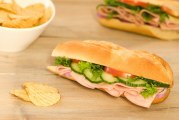 Cut ham salad baguette with crisps on a rustic table