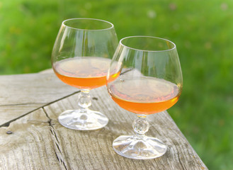 Two glasses with cognac stand on a wooden bench