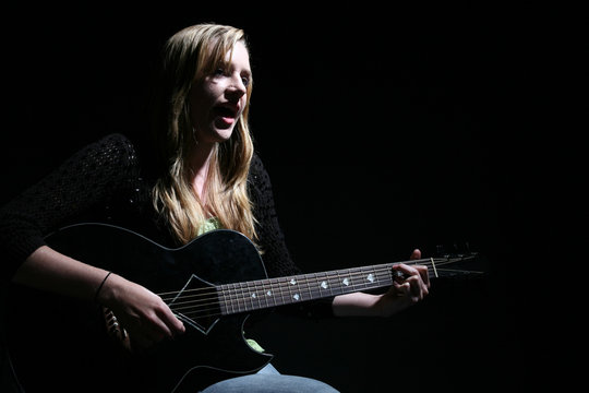 moody picture of beautiful woman playing guitar and singing
