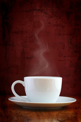 White cup with steaming hot drink on grunge background