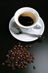 Close up of a white cup of coffee and beans on black background
