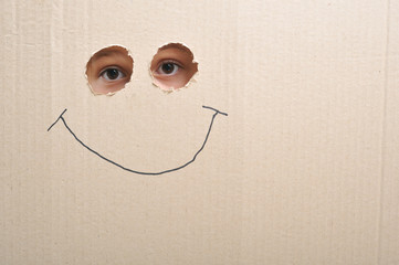 Eyes looking through two holes on a cardboard and a smile