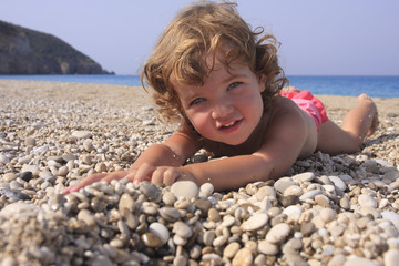 The smiling child is taking a sun-bath on the beach.