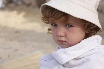 Sullen child wrapped in a towel is sitting on the beach.