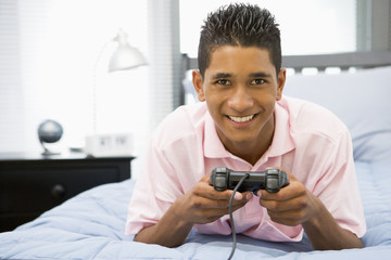 Teenage Boy Lying On Bed Playing Video Game