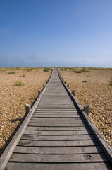 A raised wooden boardwalk across a pebble beach
