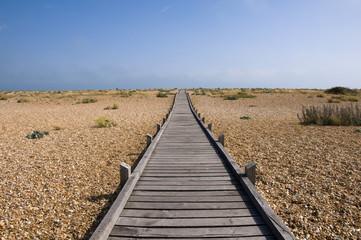 A raised wooden boardwalk across a pebble beach