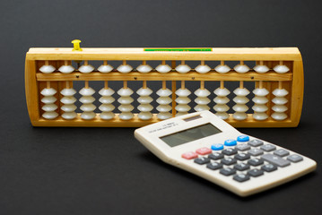 Traditional abacus and modern calculator on black background