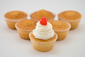 Batch of sponge cupcakes, one with cream and cherry