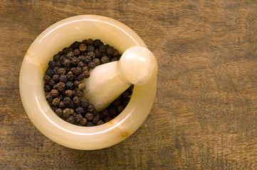 Black peppercorns, mortar and pestle on a wood cutting board