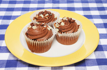 Three chocolate cup cakes on plate and table cloth