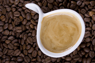 Cup of creamy espresso on coffee beans